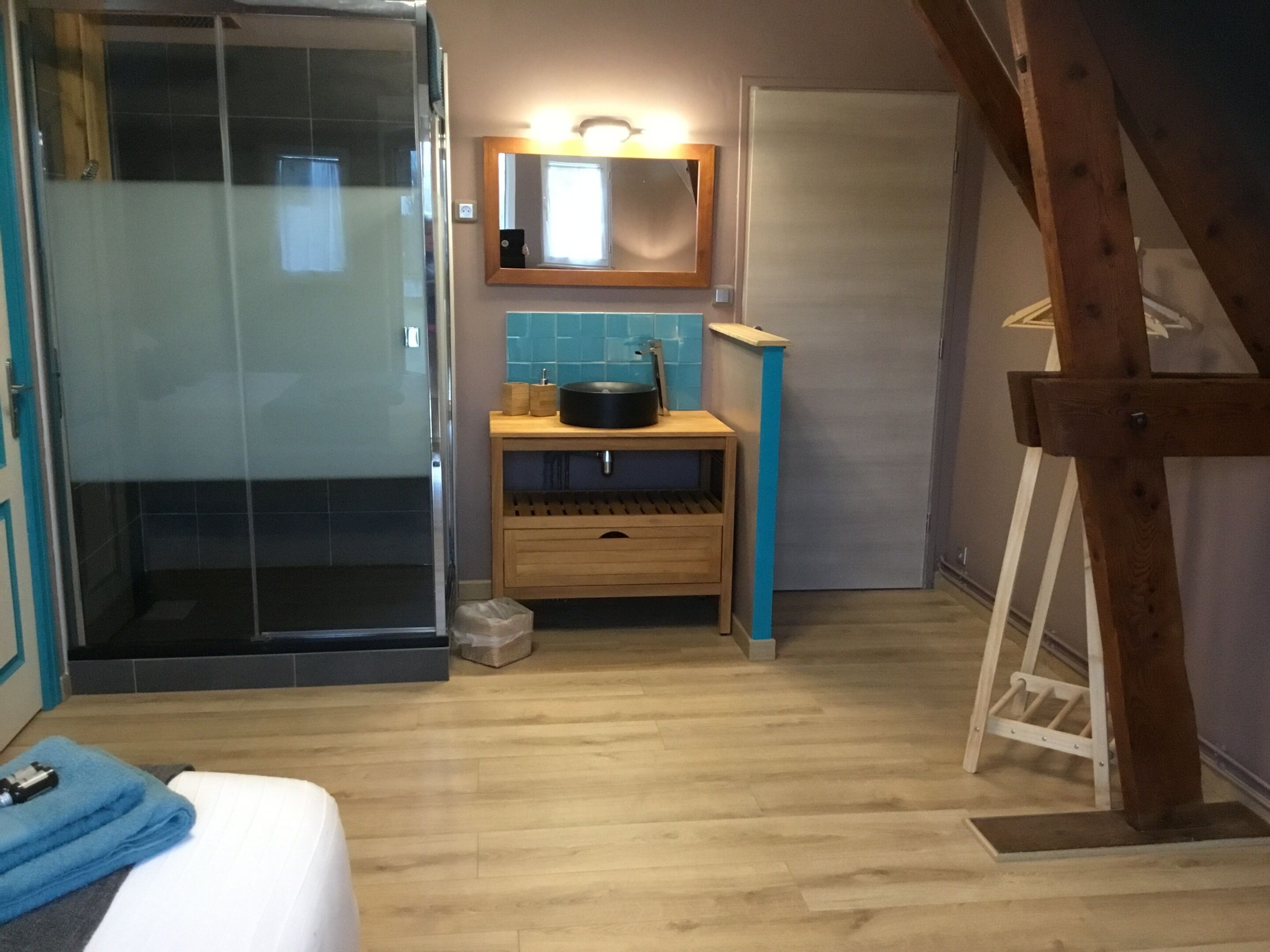 A bathroom with a glass shower enclosure, a wooden vanity with a mirror, and a wooden ladder.