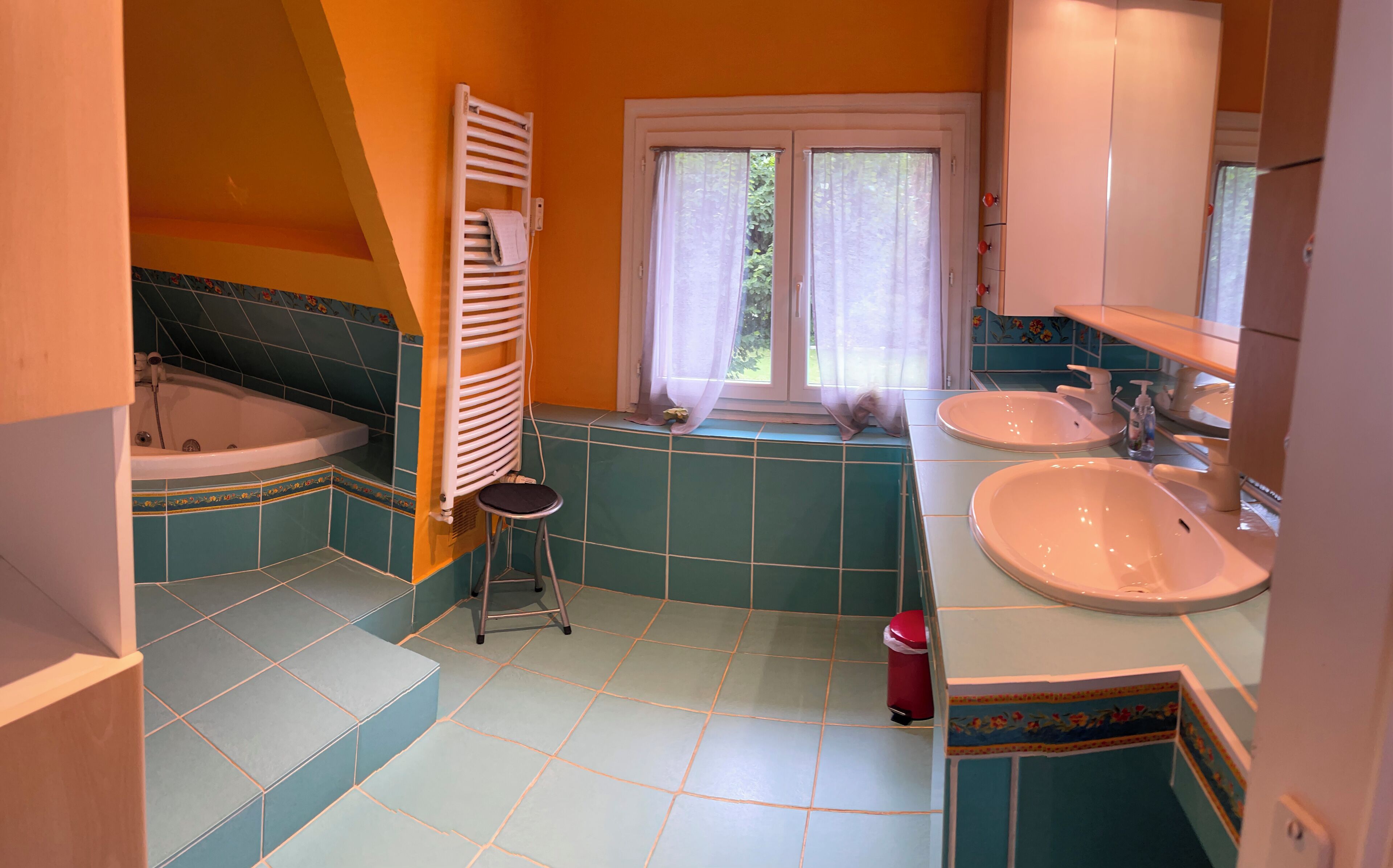 A bathroom with a bathtub, two sinks, a window with curtains, and a towel rack.