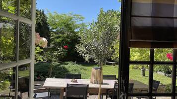 A patio area with a table and chairs, a potted plant, and a view of a garden and cemetery.