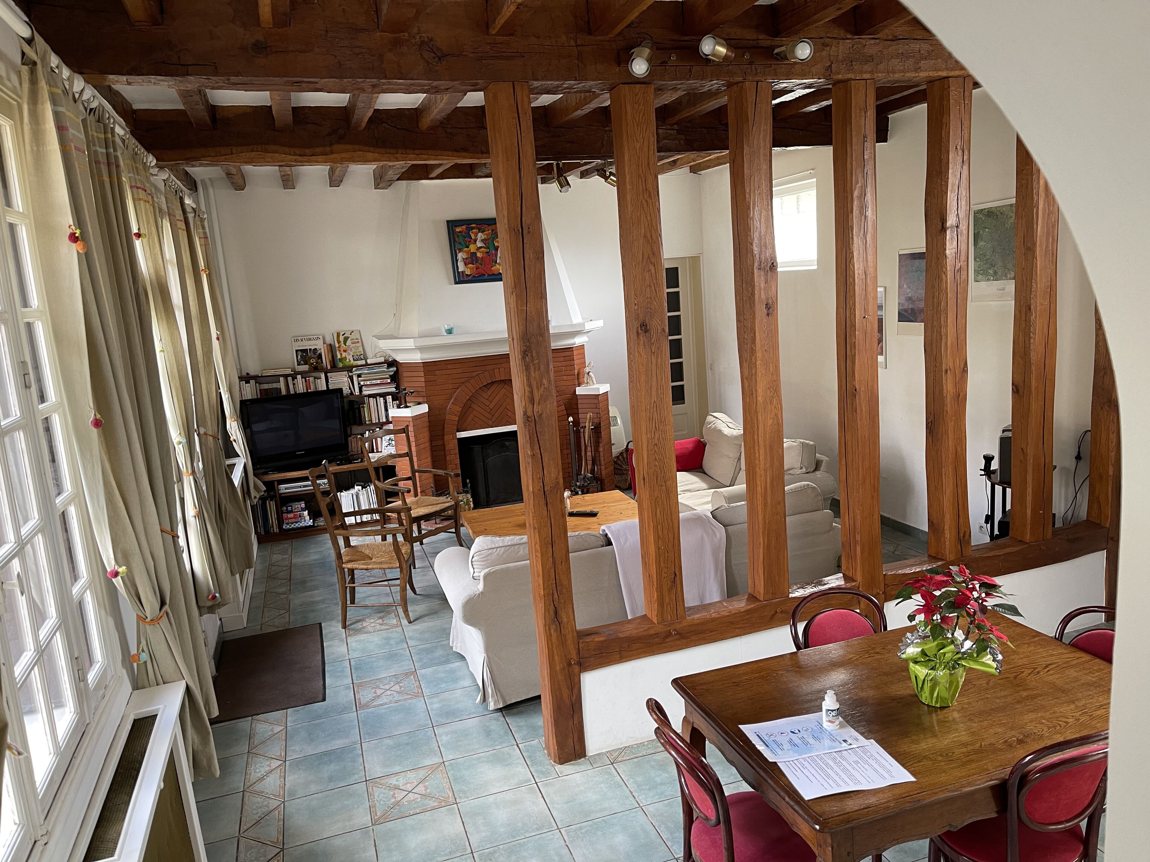 A cozy living room with a fireplace, wooden beams, a television, and a dining area with a table and chairs.