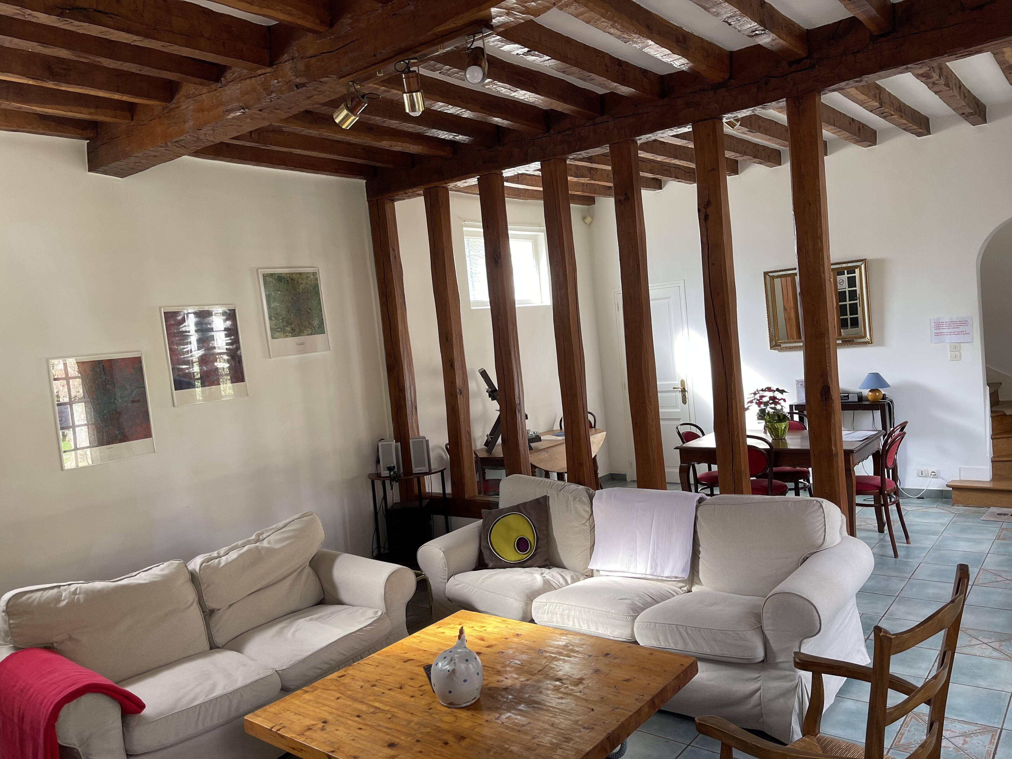 Amplia sala de estar con techo alto y vigas de madera a la vista, que incluye un conjunto de sofás, una mesa de centro de madera y un comedor al fondo.
