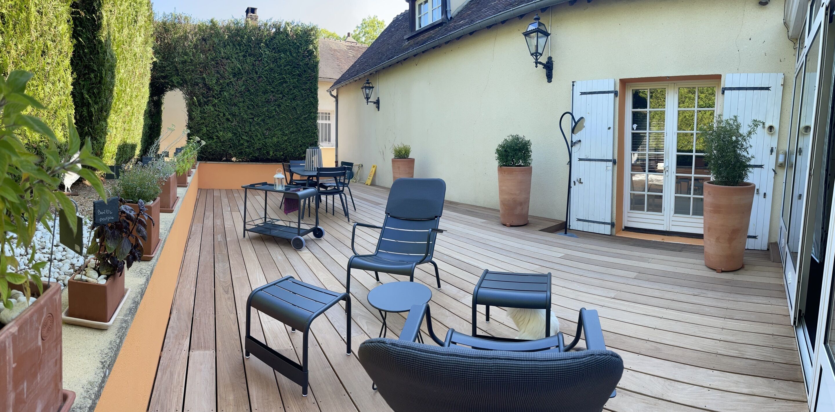 A wooden deck with outdoor furniture, potted plants, and a white door with shutters.