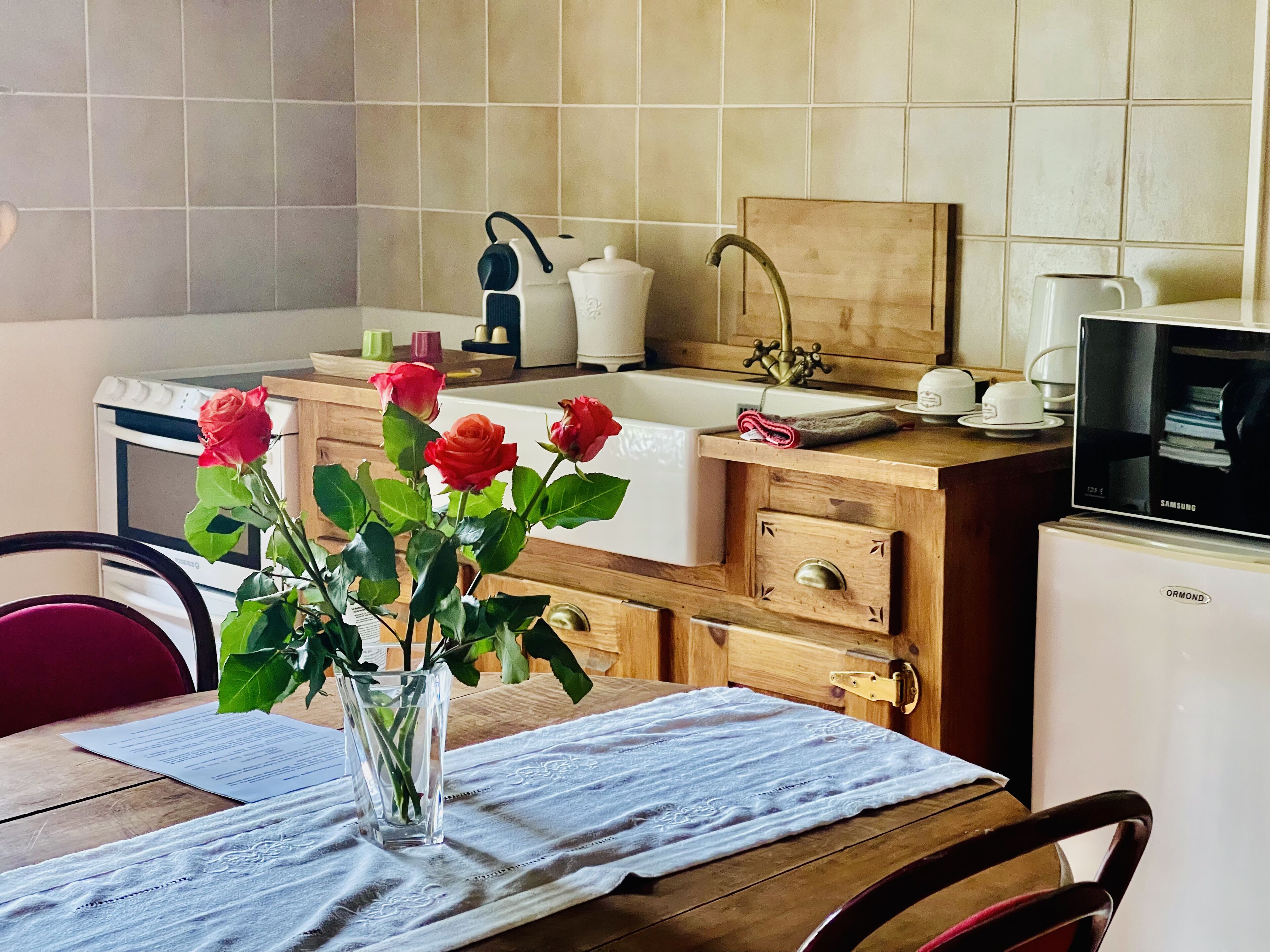 Une cuisine avec un plan de travail en bois, un évier, un four à micro-ondes et un vase rempli de roses posé sur la table.