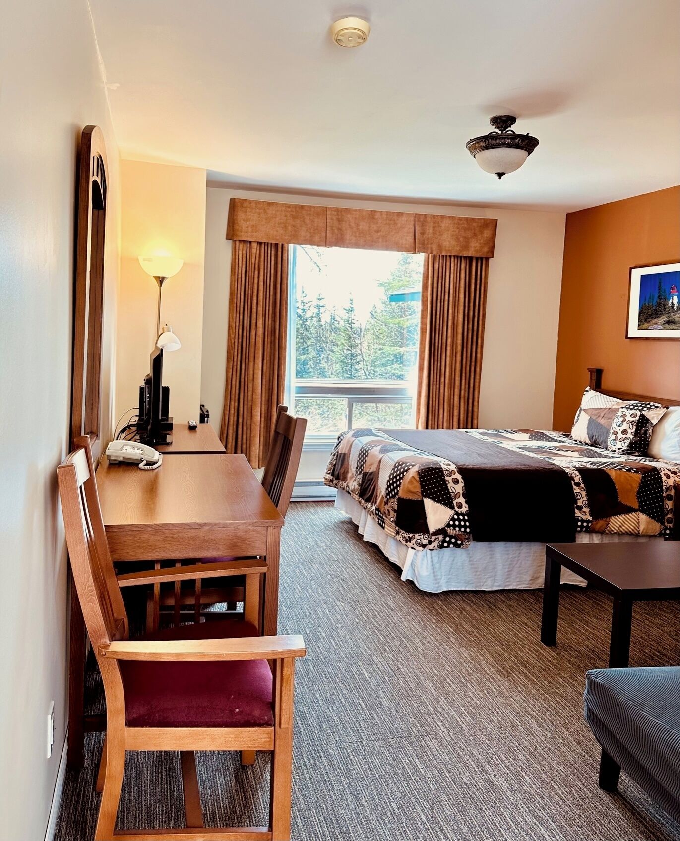 A hotel room with a bed, a desk, a chair, a lamp, and a window with curtains.