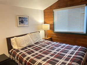 A bedroom with a bed, a nightstand, a lamp, a window with blinds, and a framed picture on the wall. - Best Northern Motel and Restaurant (Wawa)