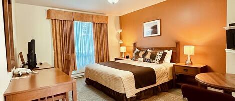 Una habitación de hotel con cama, escritorio, silla, televisor y lámpara.
