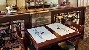 Zona de bar con mobiliario de madera, un televisor montado en la pared y un muro de ladrillo al fondo.