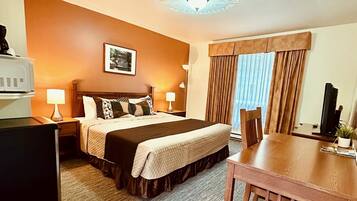 A hotel room with a bed, bedside tables, a desk, a chair, a television, and a window with curtains.
