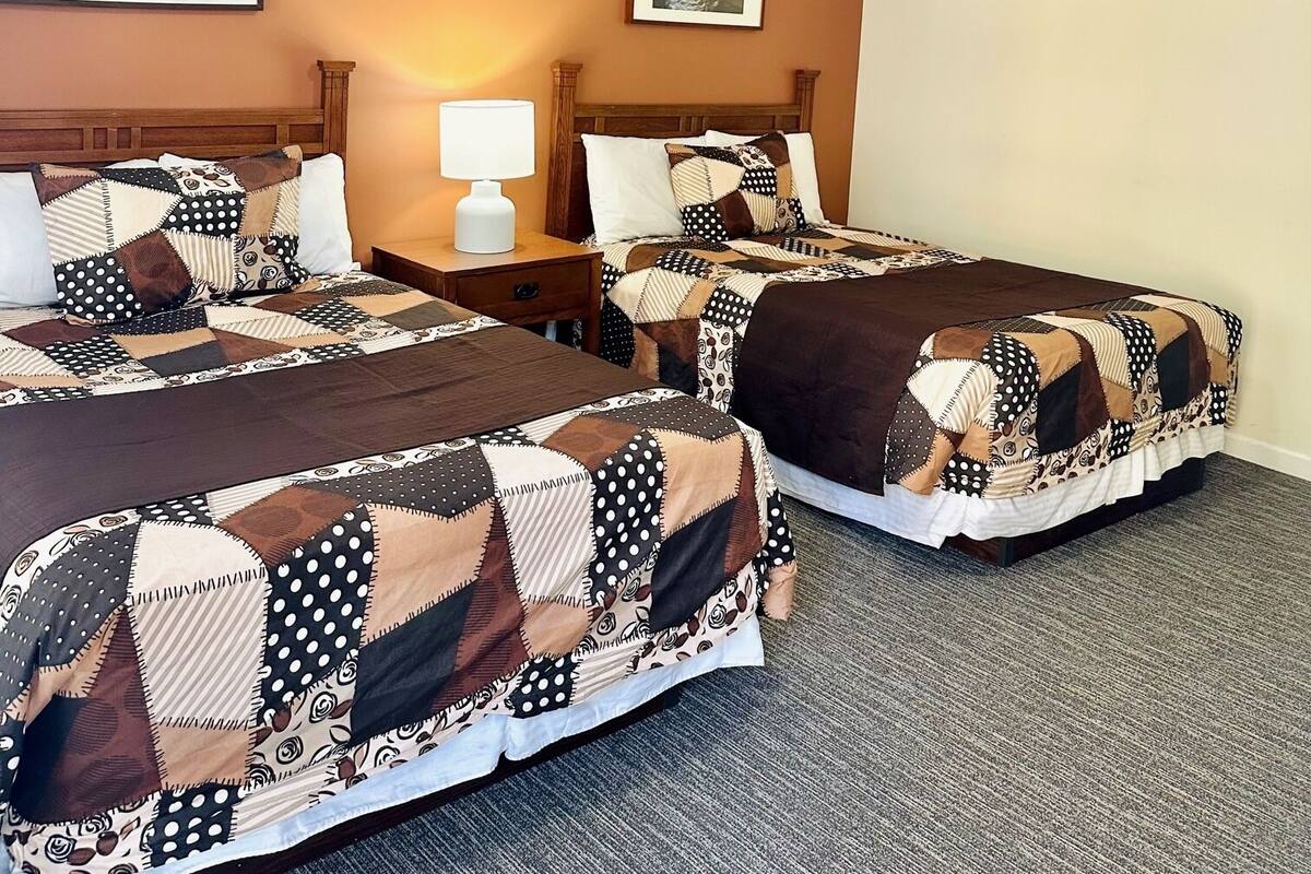A hotel room with two beds, a nightstand, a lamp, and two framed pictures on the wall.