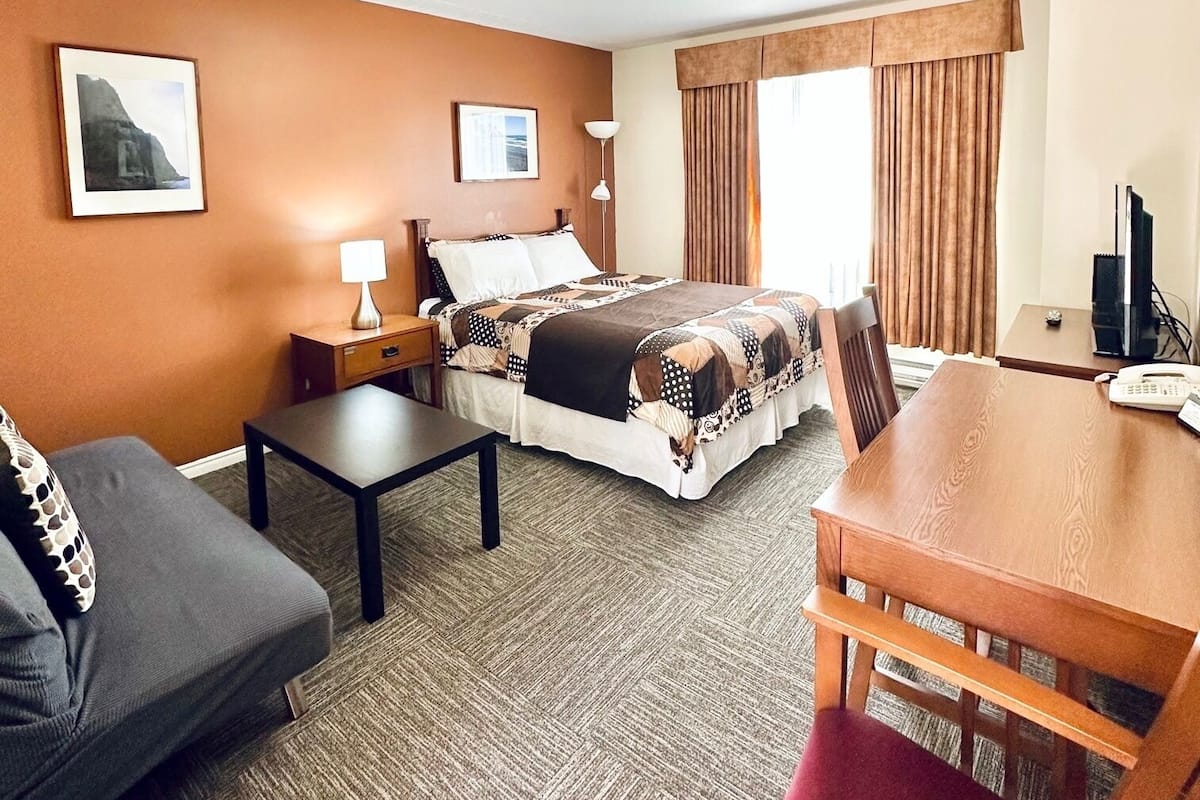 A hotel room with a bed, a desk, a chair, a sofa, a lamp, a TV, and two framed pictures on the wall.