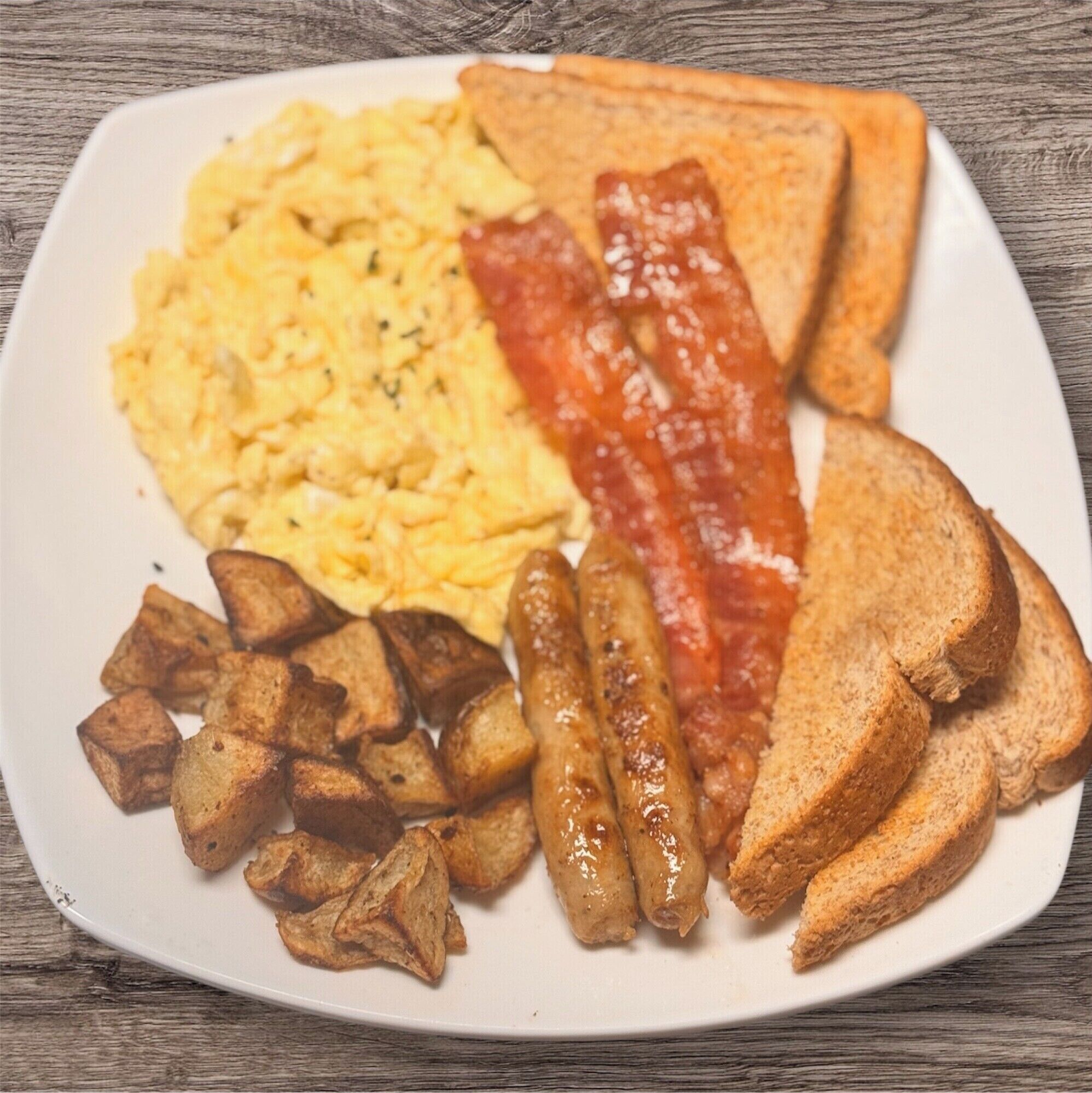 A plate with scrambled eggs, bacon, toast, and roasted potatoes.