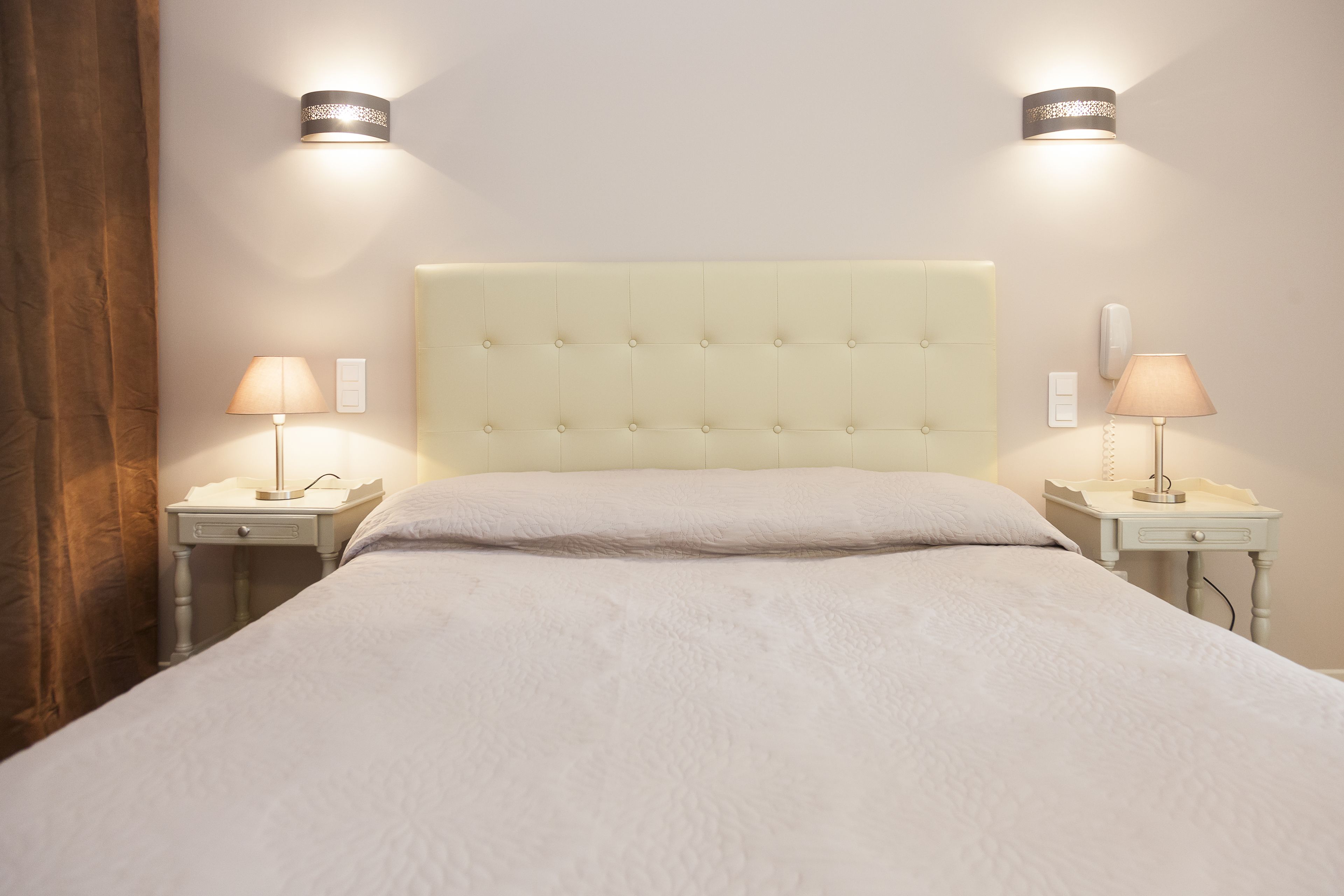 Una cama bien hecha con cabecera capitonada, dos lámparas de noche y un teléfono en la mesita.