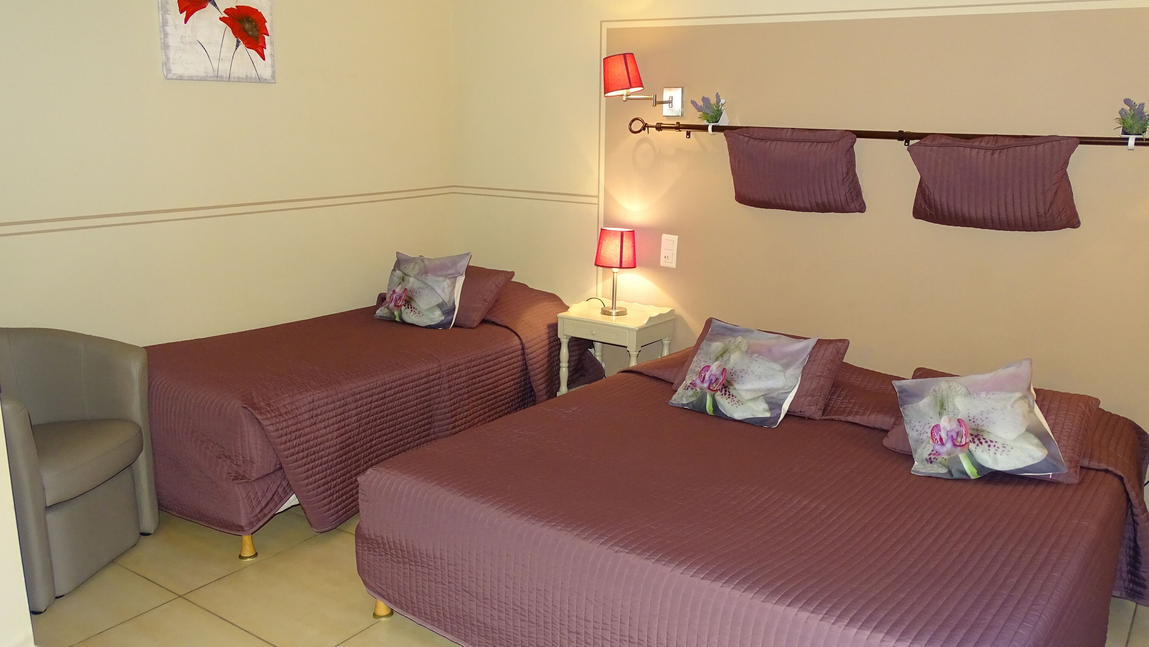Une chambre avec deux lits, chacun agrémenté d’oreillers assortis et d’une table de chevet avec une lampe. On y trouve également une chaise et une étagère murale décorative.