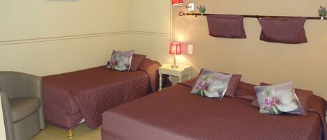 Une chambre avec deux lits, chacun agrémenté d’oreillers assortis et d’une table de chevet avec une lampe. On y trouve également une chaise et une étagère murale décorative.