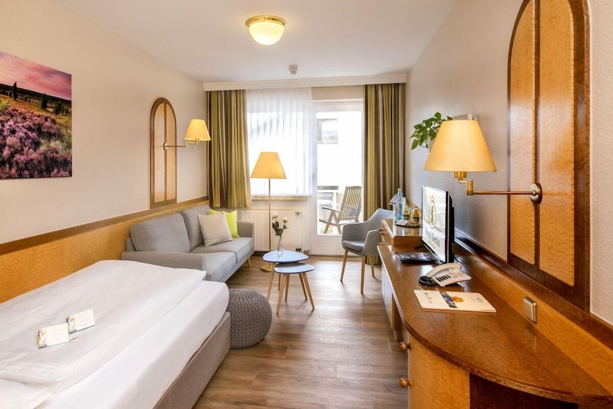 A hotel room with a bed, sofa, two small tables, a desk with a telephone, and a TV.