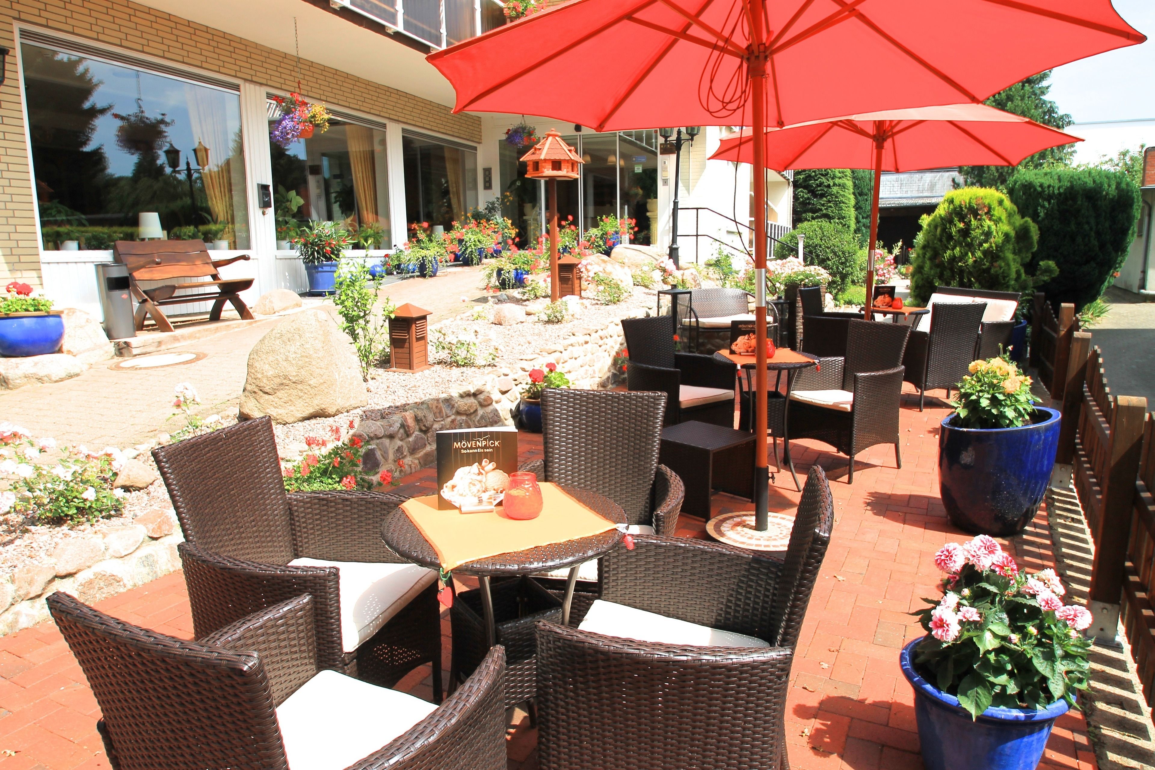 An outdoor patio area with wicker furniture, red umbrellas, and potted plants.