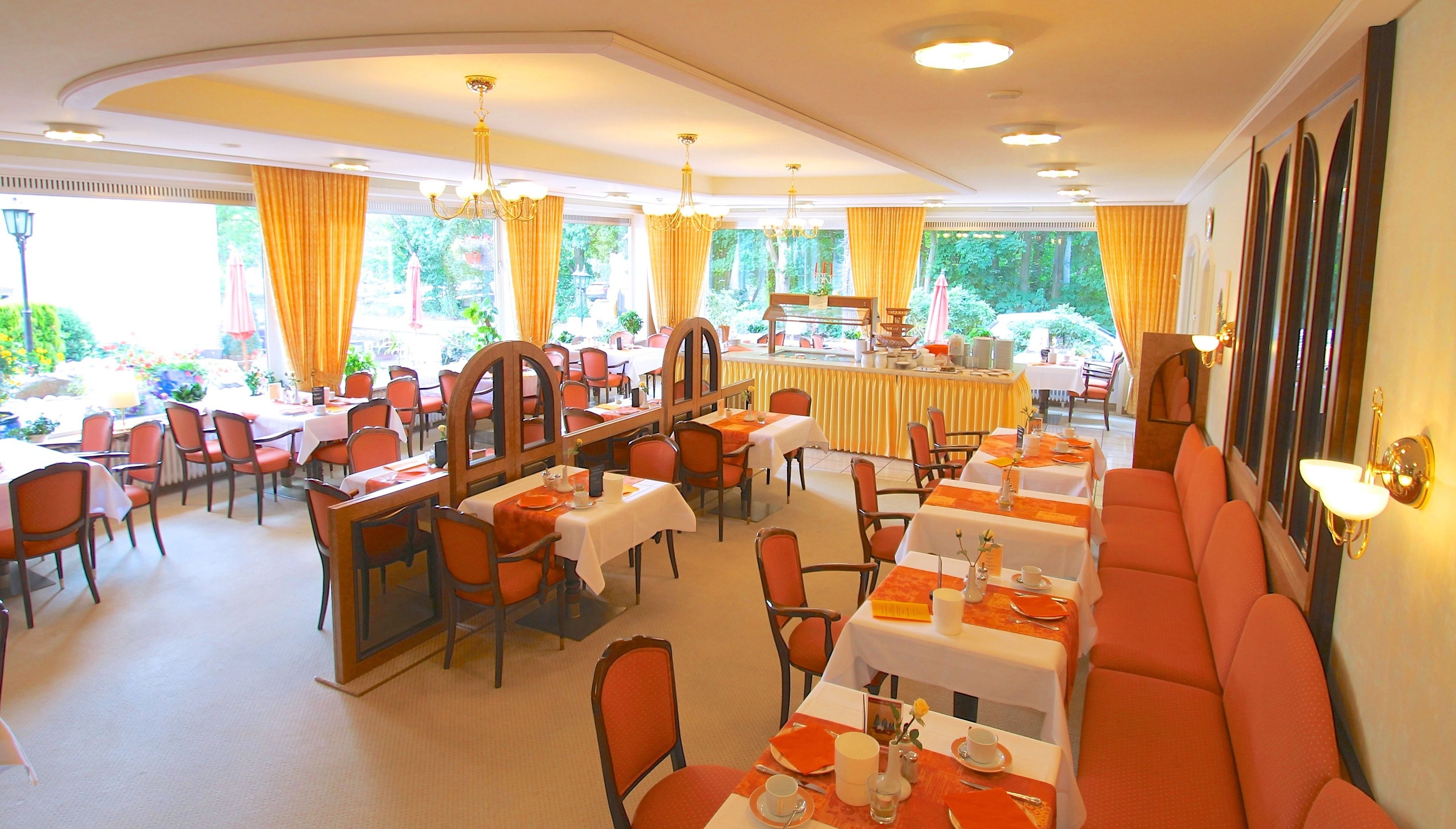 A restaurant with multiple tables and chairs, a bar area, and large windows with curtains.