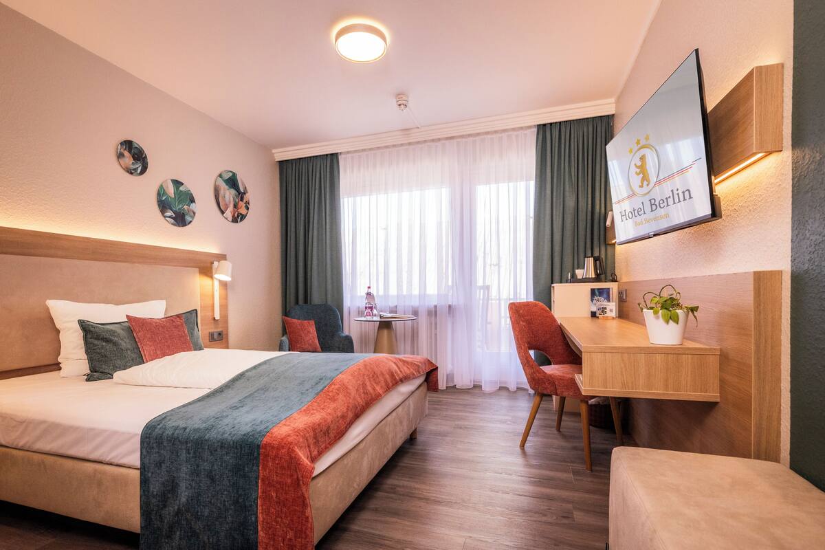 A hotel room with a bed, desk, chair, and a TV on the wall.