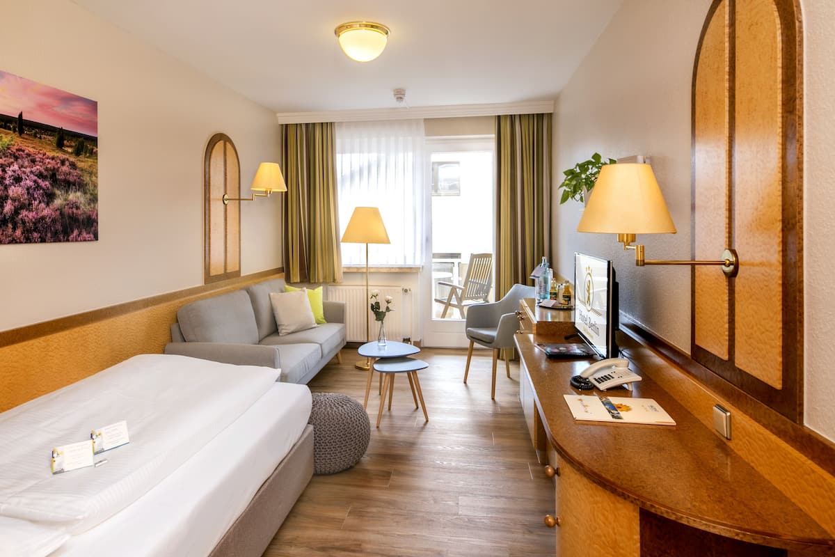 A hotel room with a bed, a sofa, a desk with a lamp, a chair, and a television.
