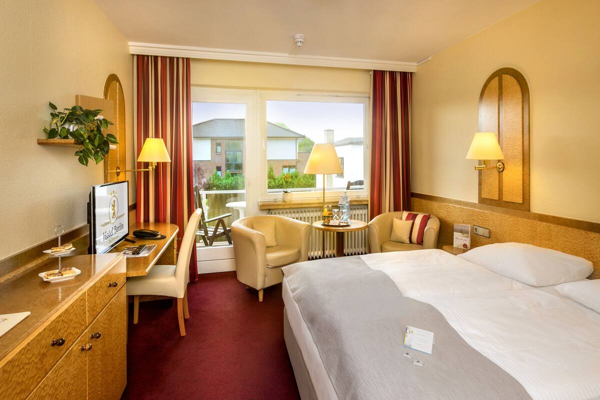 A hotel room with a bed, desk, chairs, and a view of the outside.