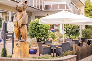 Eine Holzstatue eines BĂ€ren, Sitzgelegenheiten im Freien mit Sonnenschirmen und ein Schild fĂŒr Hotel Berlin.