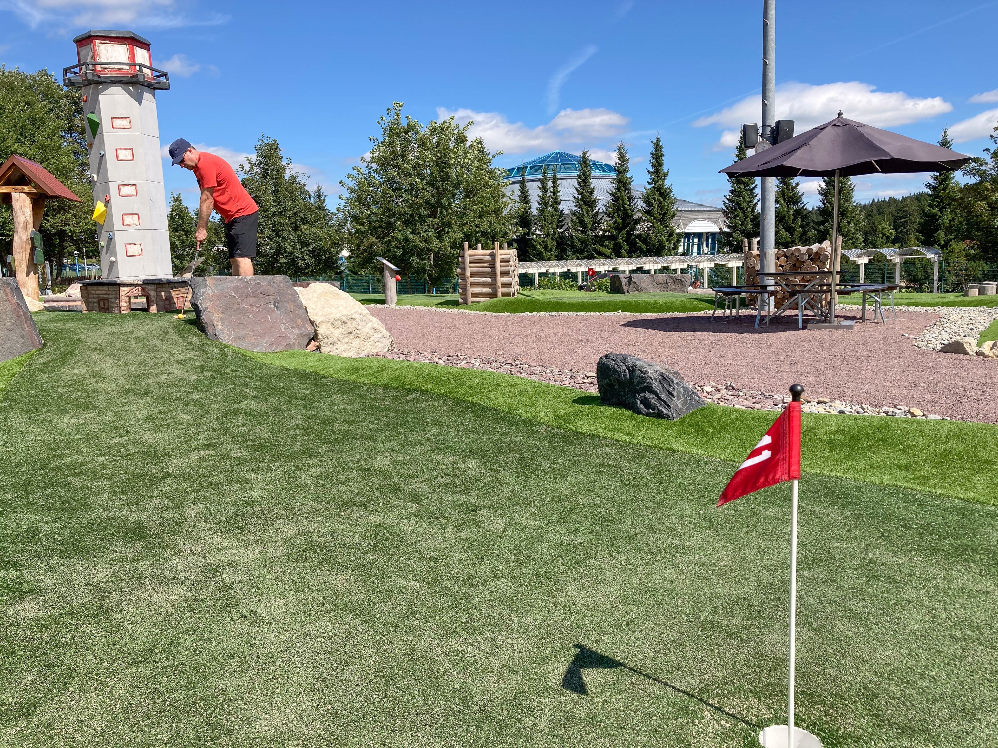 Een golfbaan met een vlaggenstok, een vuurtoren en een prieel.