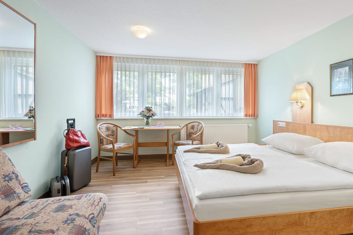 Ein Hotelzimmer mit Bett, Schreibtisch, zwei Stühlen, einem kleinen Tisch mit einer Vase und einem Koffer.