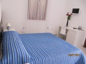 Una camera d'hotel con un letto, una scrivania, una sedia, una televisione e una finestra con tende.