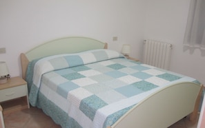 Ein Bett mit einer Steppdecke, ein Nachttisch mit einer Lampe und ein Heizkörper.