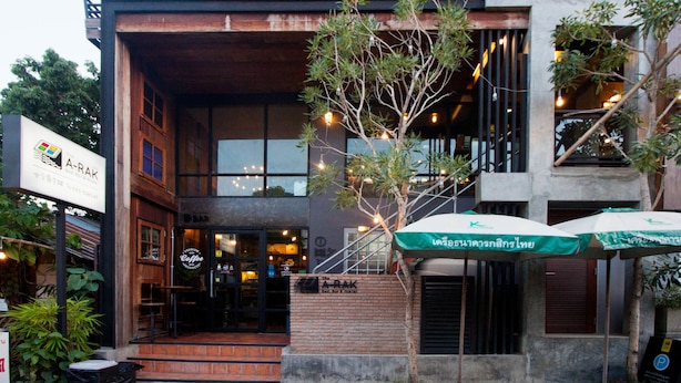 Un edificio moderno con una cafetería en la planta baja, mesas al aire libre con sombrillas y una escalera que conduce al nivel superior.