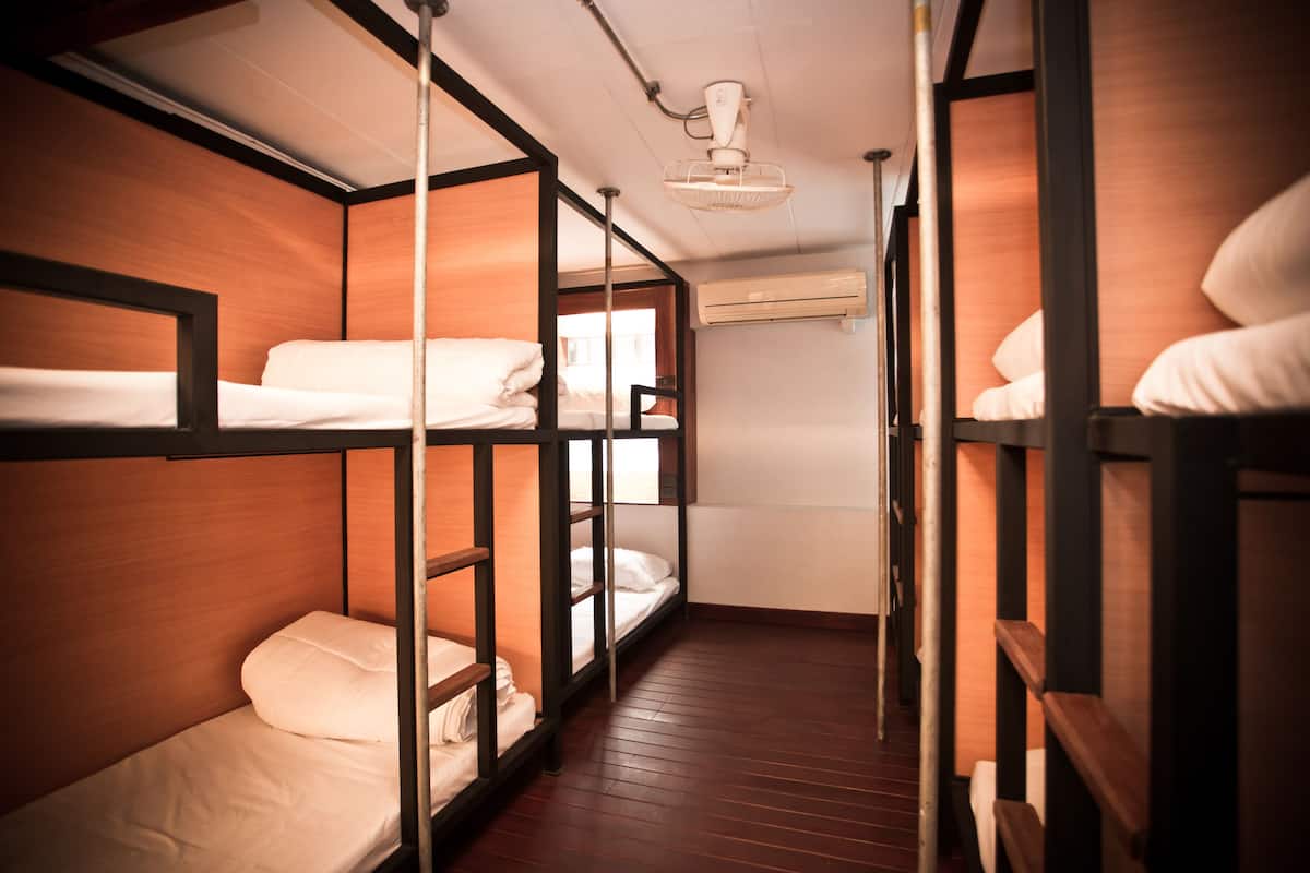 A narrow corridor with bunk beds on either side, wooden walls, and an air conditioning unit on the wall.