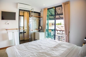Habitación de hotel con cama, televisión, baño y balcón con mesa y sillas.