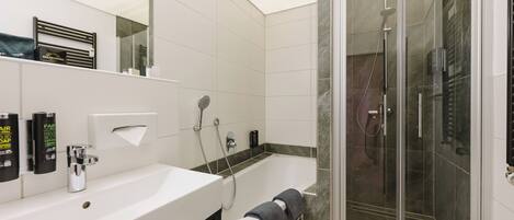 A modern bathroom with a white sink, a glass-enclosed shower, and a marble-tiled wall.