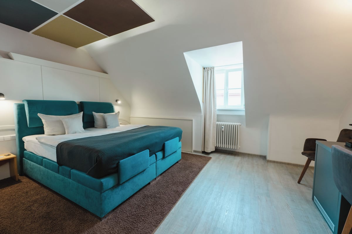 A modern bedroom with a large bed, a desk, and a window.