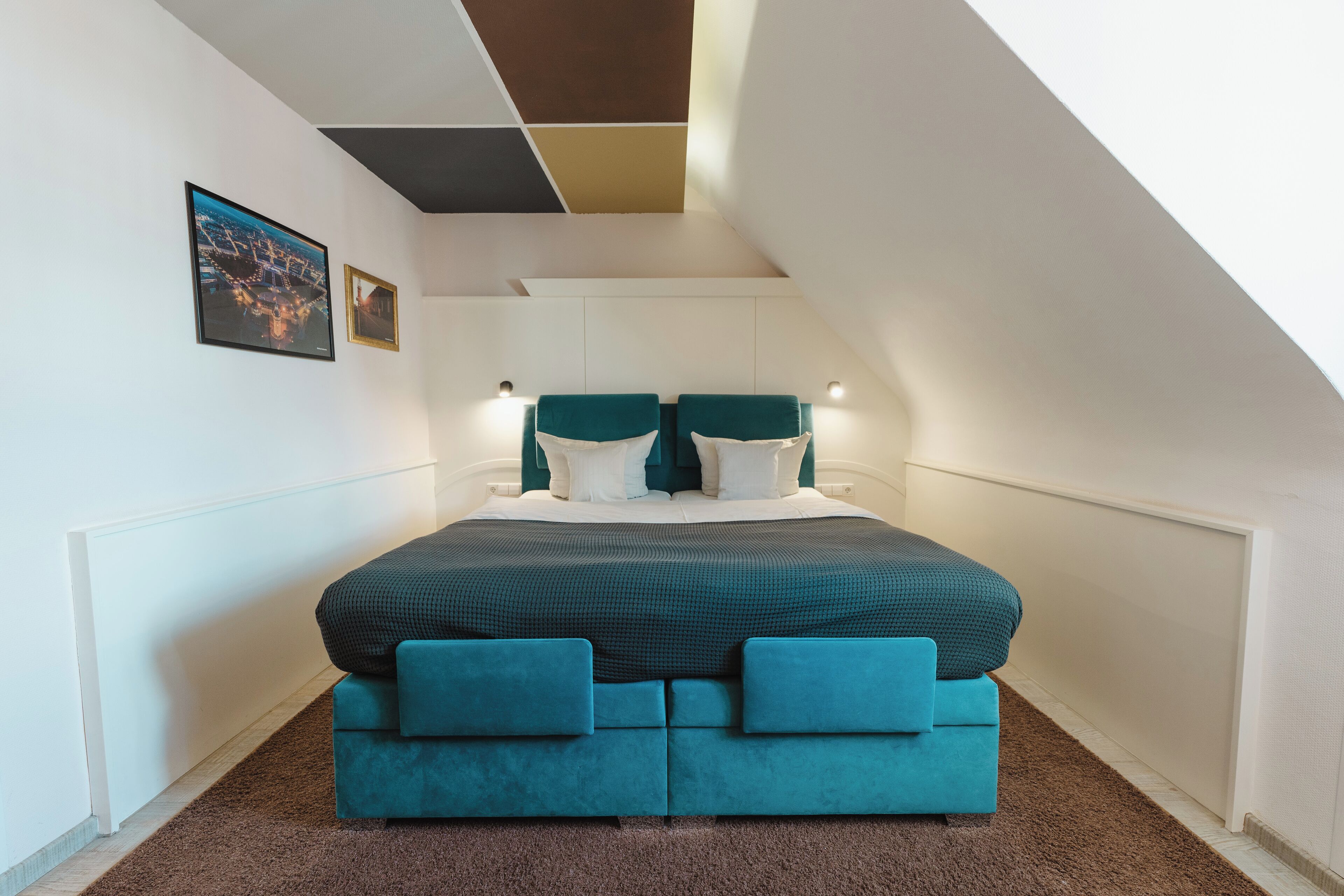 A bedroom with a large bed, a sloped ceiling, and a cityscape picture on the wall.
