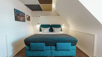 A bedroom with a large bed, a sloped ceiling, and a cityscape picture on the wall.