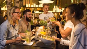 Un grupo de personas cenando en un restaurante con una decoración moderna, incluyendo una zona de bar al fondo.