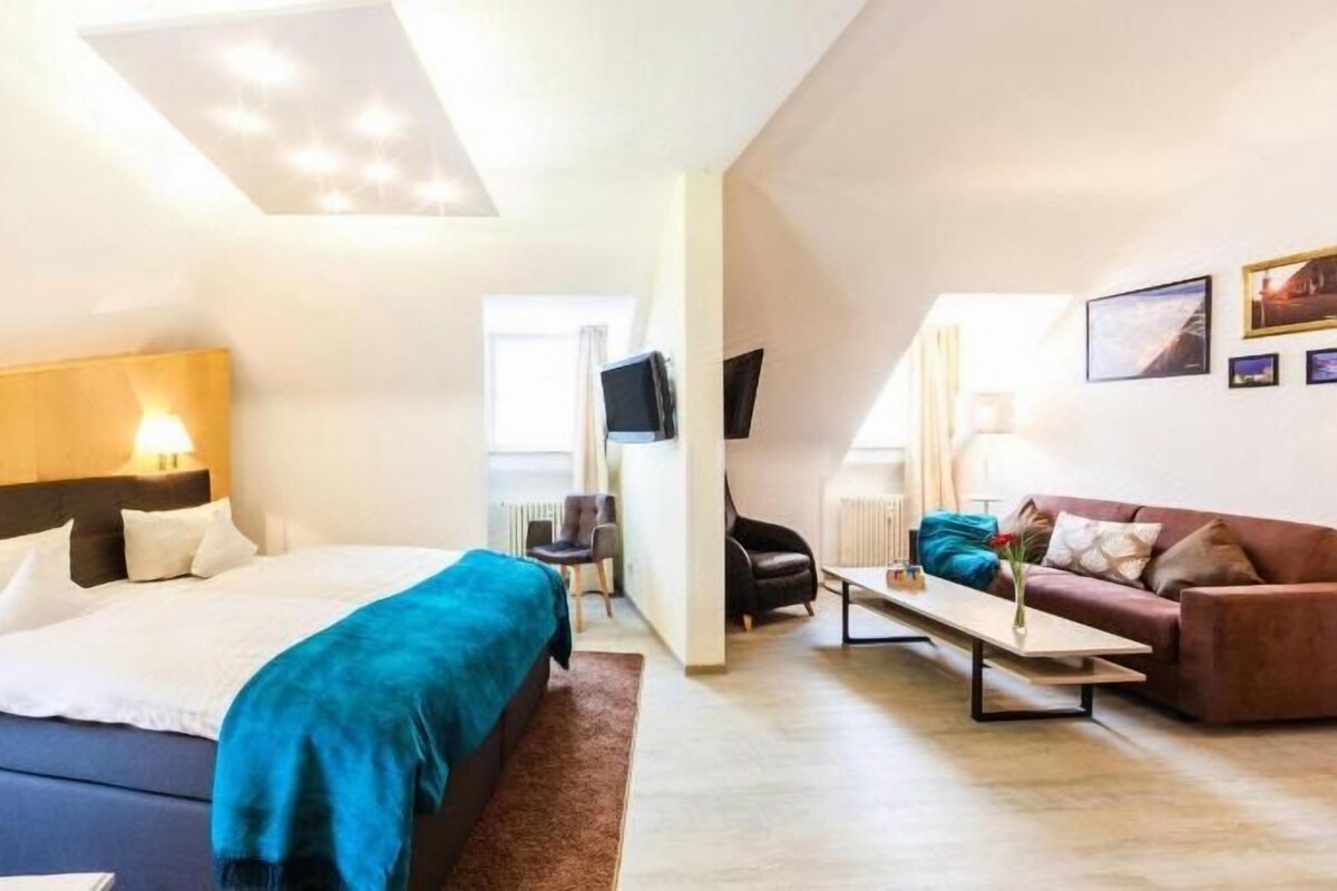 A modern hotel room with a large bed, a sofa, a TV, and a flat-screen TV mounted on the wall.