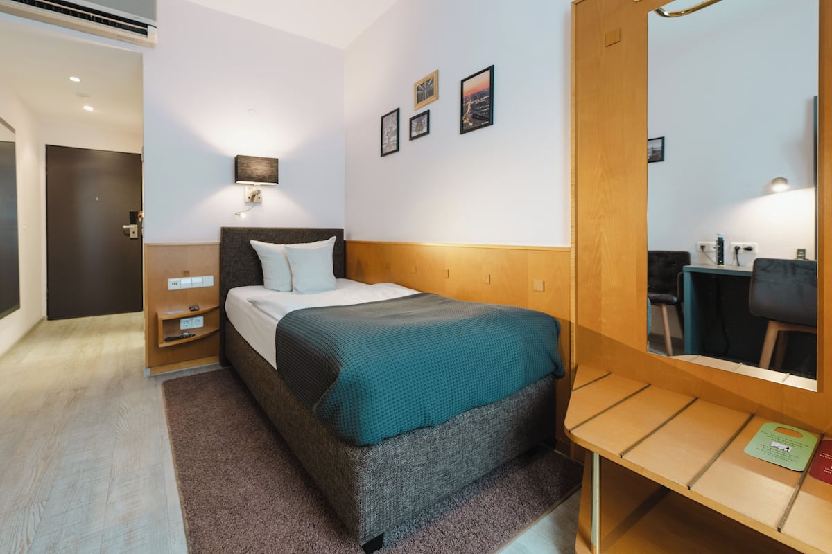 A modern hotel room with a large bed, a bedside table, a desk, and a mirror.
