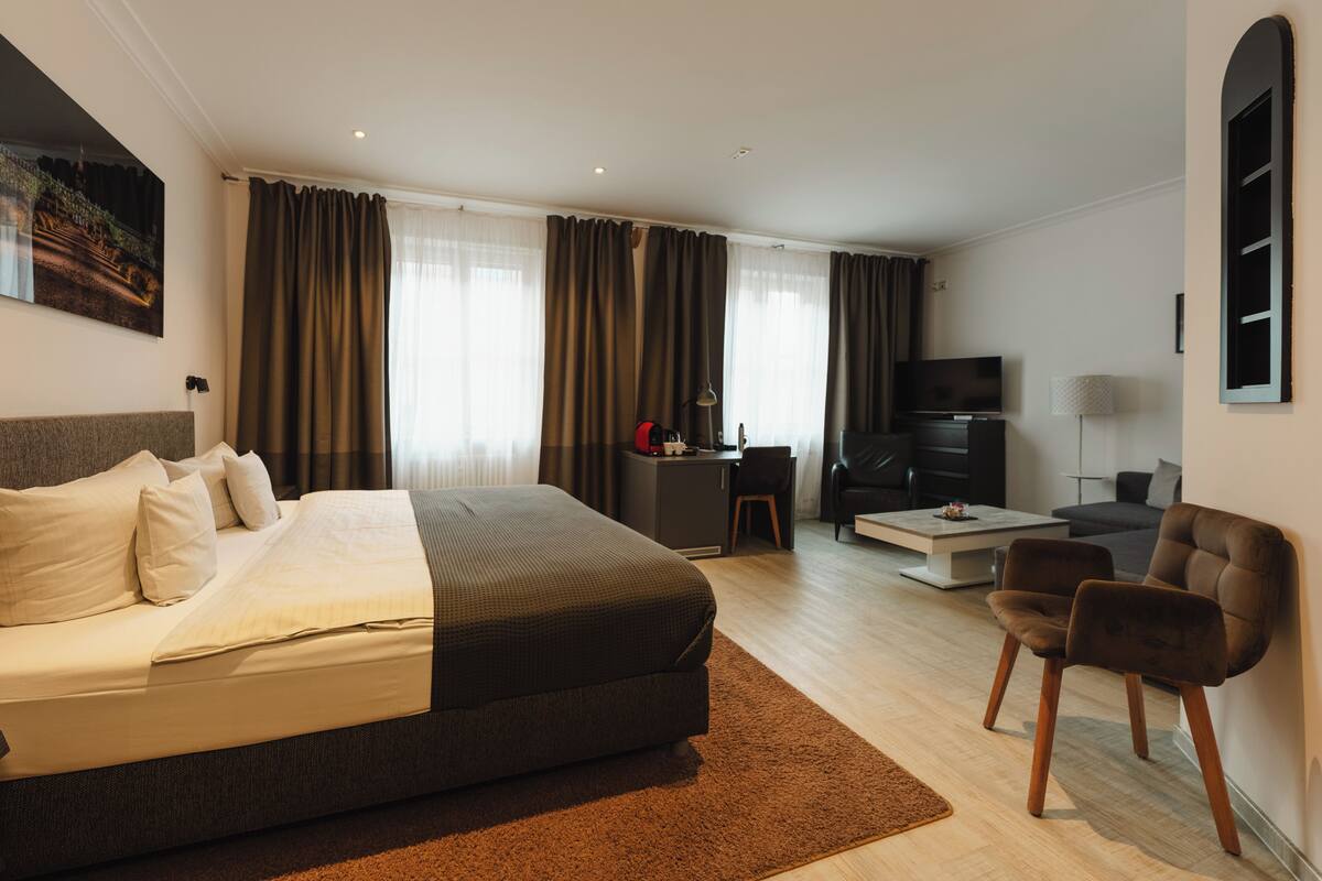 A hotel room with a bed, a desk, a TV, a sofa, and a chair.