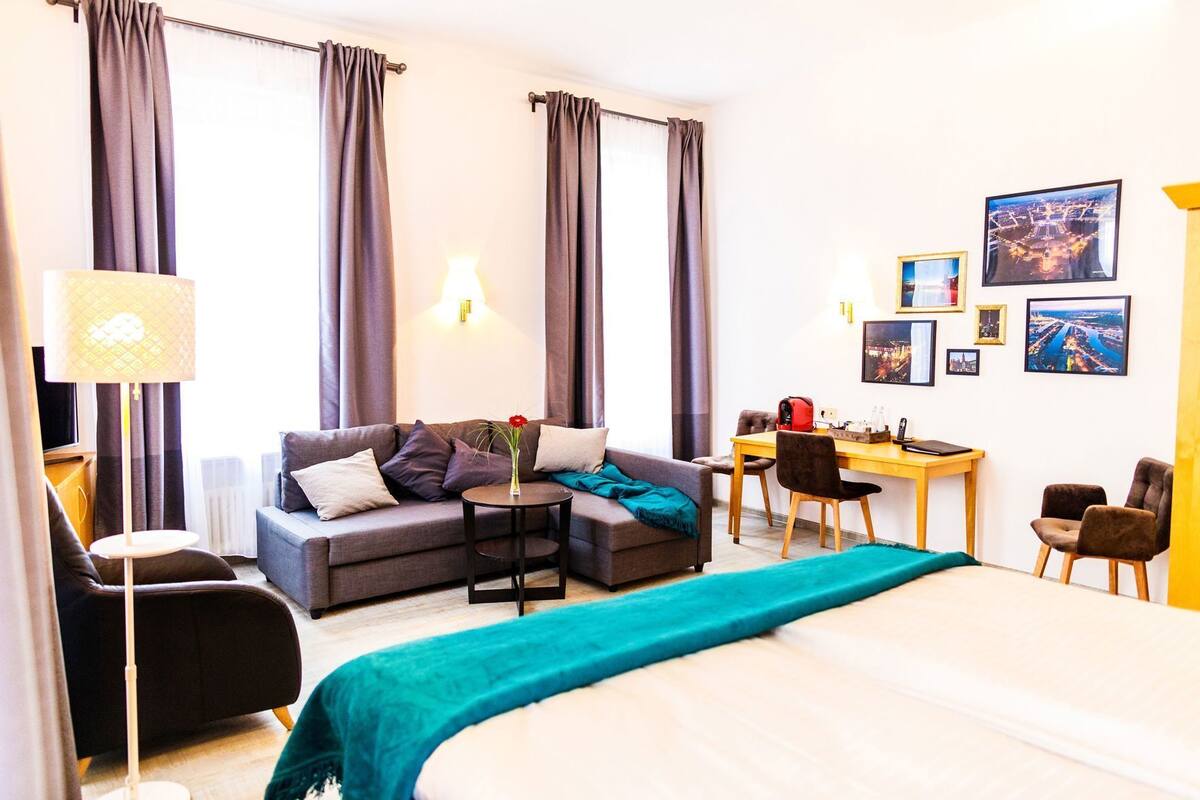 A modern hotel room with a bed, sofa, desk, and chairs.