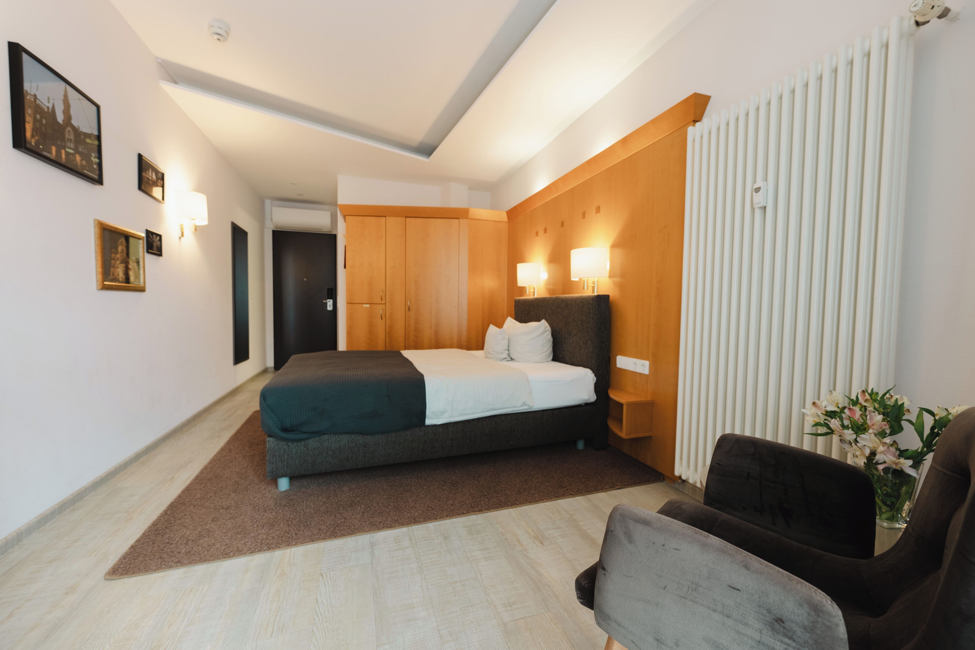 Una habitación de hotel moderna con cama, una silla, un armario de madera y un radiador.