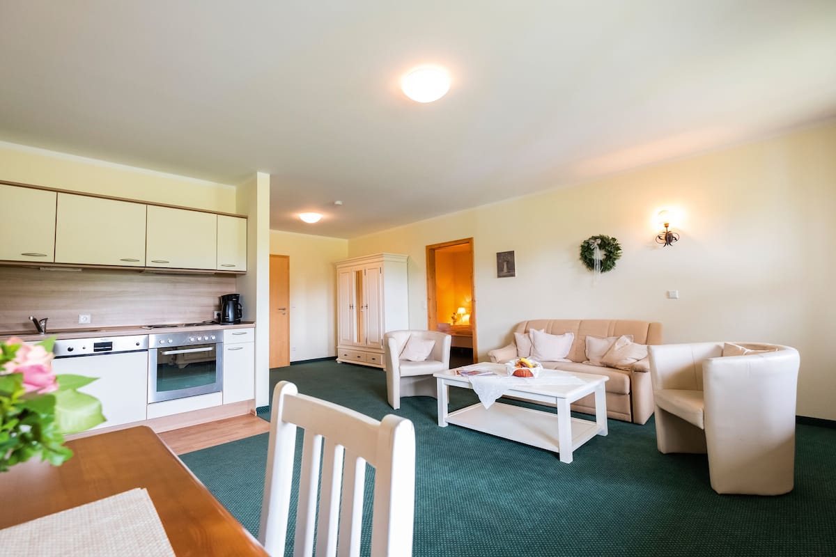 Una sala de estar moderna con cocina, muebles blancos y alfombra verde.