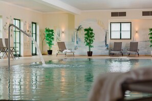 Una piscina interior con fuente, sillas de descanso y murales decorativos.