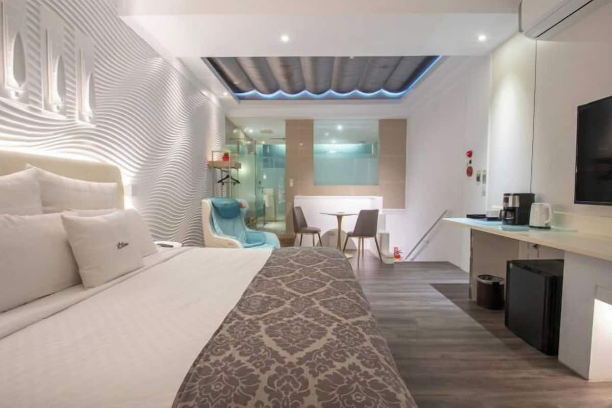A modern hotel room with a large bed, a desk, and a seating area.