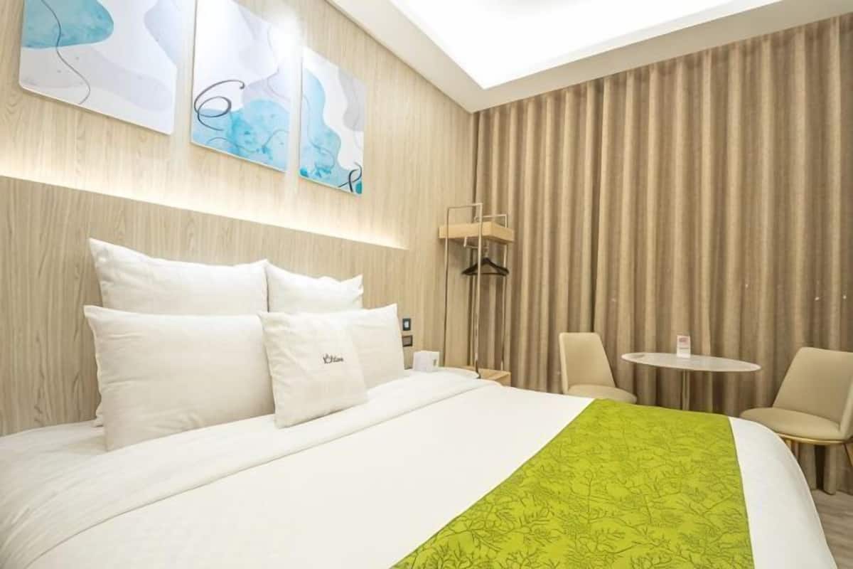 A hotel room with a large bed, a bedside table, a chair, a small round table, and a view of the sky through a skylight.