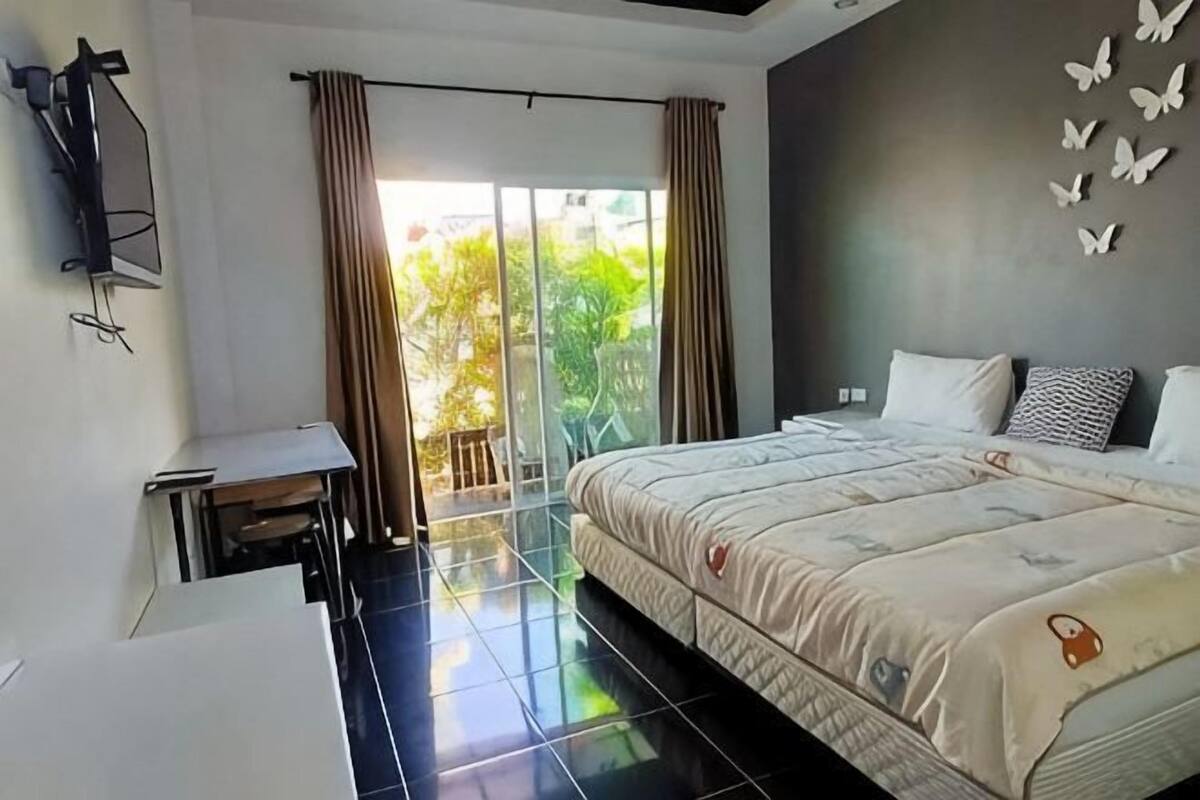 Quarto com cama, escrivaninha, televisão e varanda com cortinas.