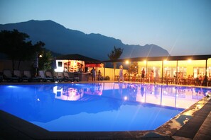 Ein Pool mit Liegestühlen und einer Bar, umgeben von Bergen.