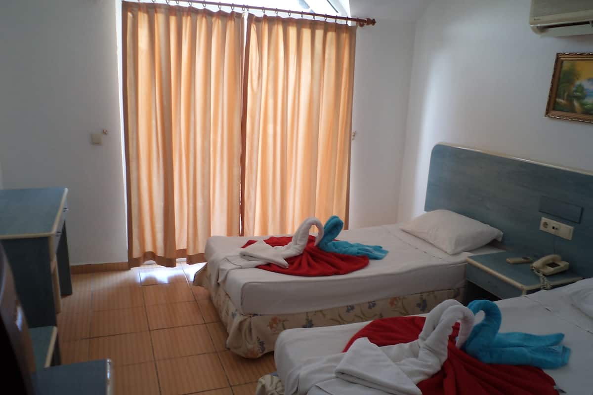 A hotel room with two beds, a desk, a nightstand, and a window with curtains.