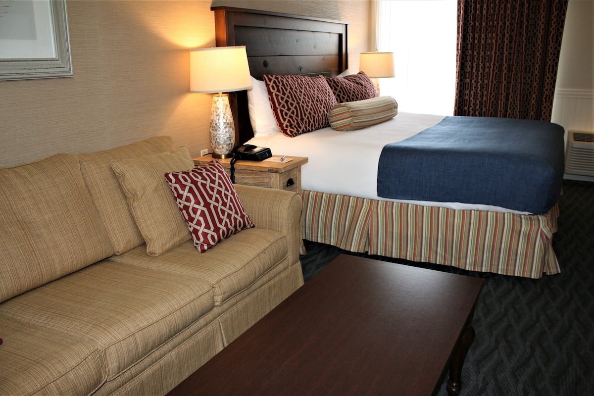 A hotel room with a bed, a sofa, a nightstand, and a lamp.